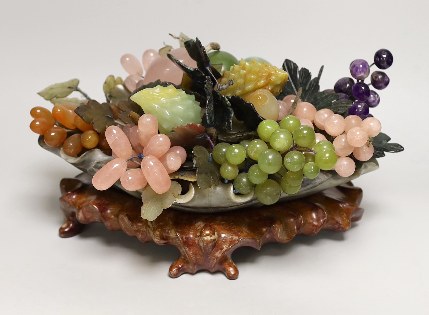 A Chinese soapstone dish of hardstone fruit on hardwood stand, 38cm wide